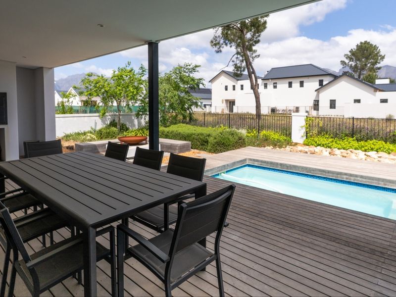 Covered outdoor patio featuring timber decking, a built-in fireplace, and direct access to a private swimming pool and landscaped garden area.