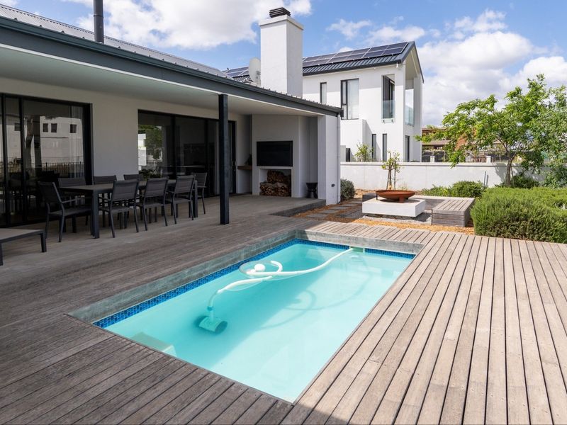 Outdoor entertainment area featuring a swimming pool, extensive timber decking, a covered patio with a built-in fireplace, and landscaped garden surroundings.
