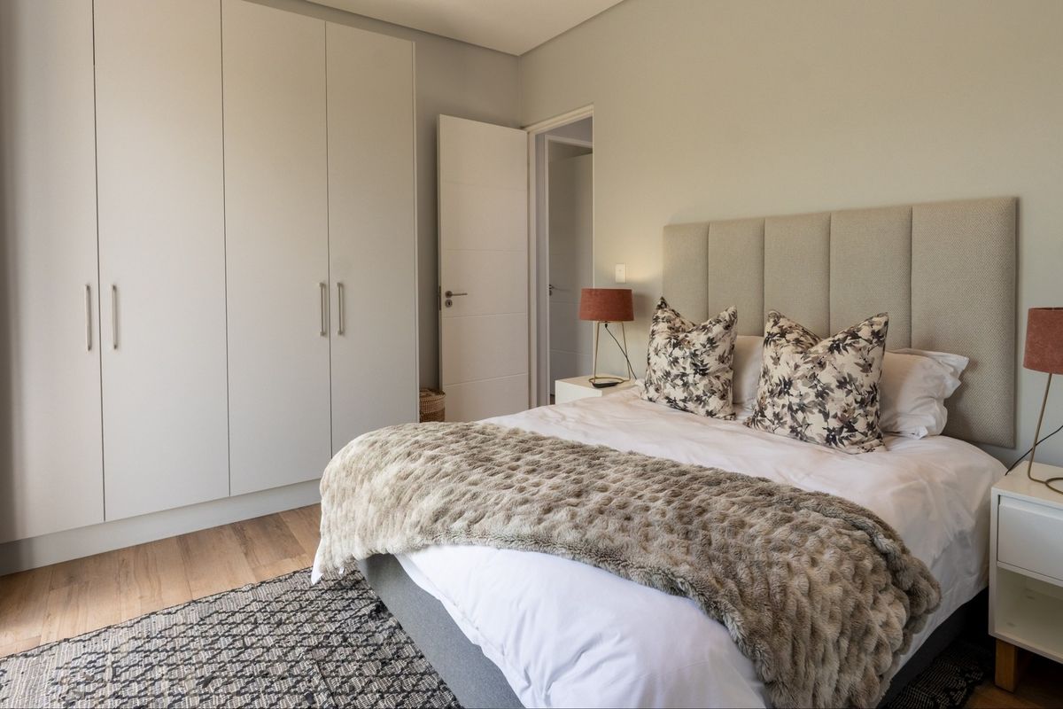 A well-maintained bedroom featuring neutral tones, built-in cupboards, laminate flooring, and a modern upholstered headboard.