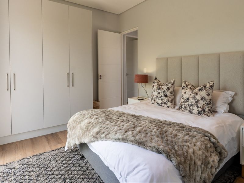 A well-maintained bedroom featuring neutral tones, built-in cupboards, laminate flooring, and a modern upholstered headboard.