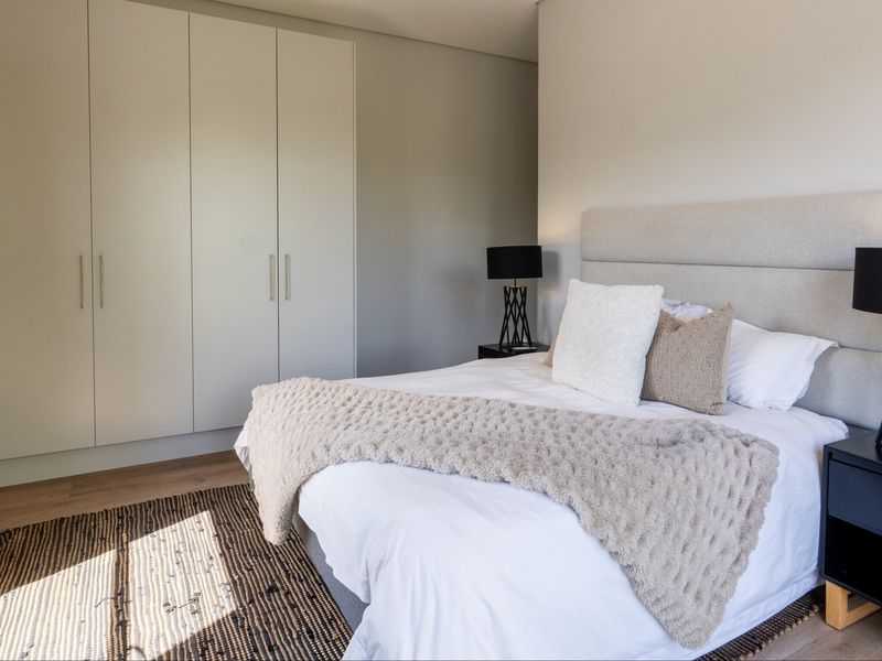 A well-maintained bedroom featuring neutral tones, modern built-in cupboards, and light laminate flooring, creating a clean and inviting atmosphere.