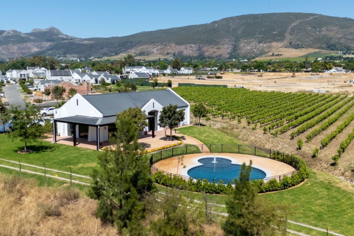 Aerial view of a modern farmhouse-style property featuring a swimming pool, covered patio, and adjacent vineyard with scenic mountain views.