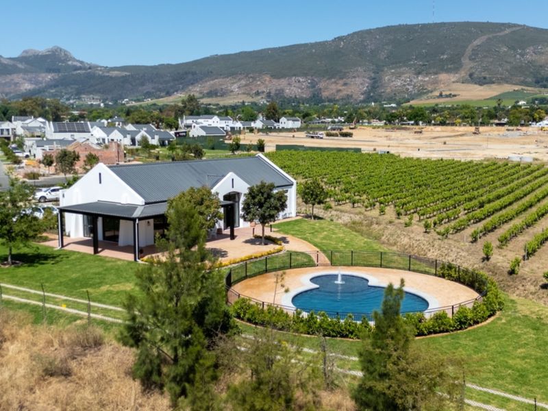 Aerial view of a modern farmhouse-style property featuring a swimming pool, covered patio, and adjacent vineyard with scenic mountain views.