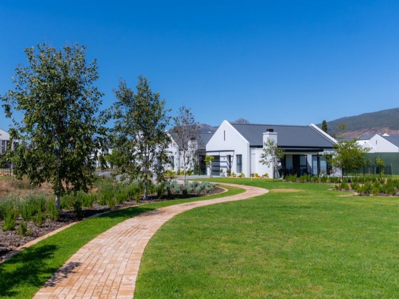 A well-maintained modern house exterior featuring a brick pathway leading through a landscaped garden towards the front entrance and garage.