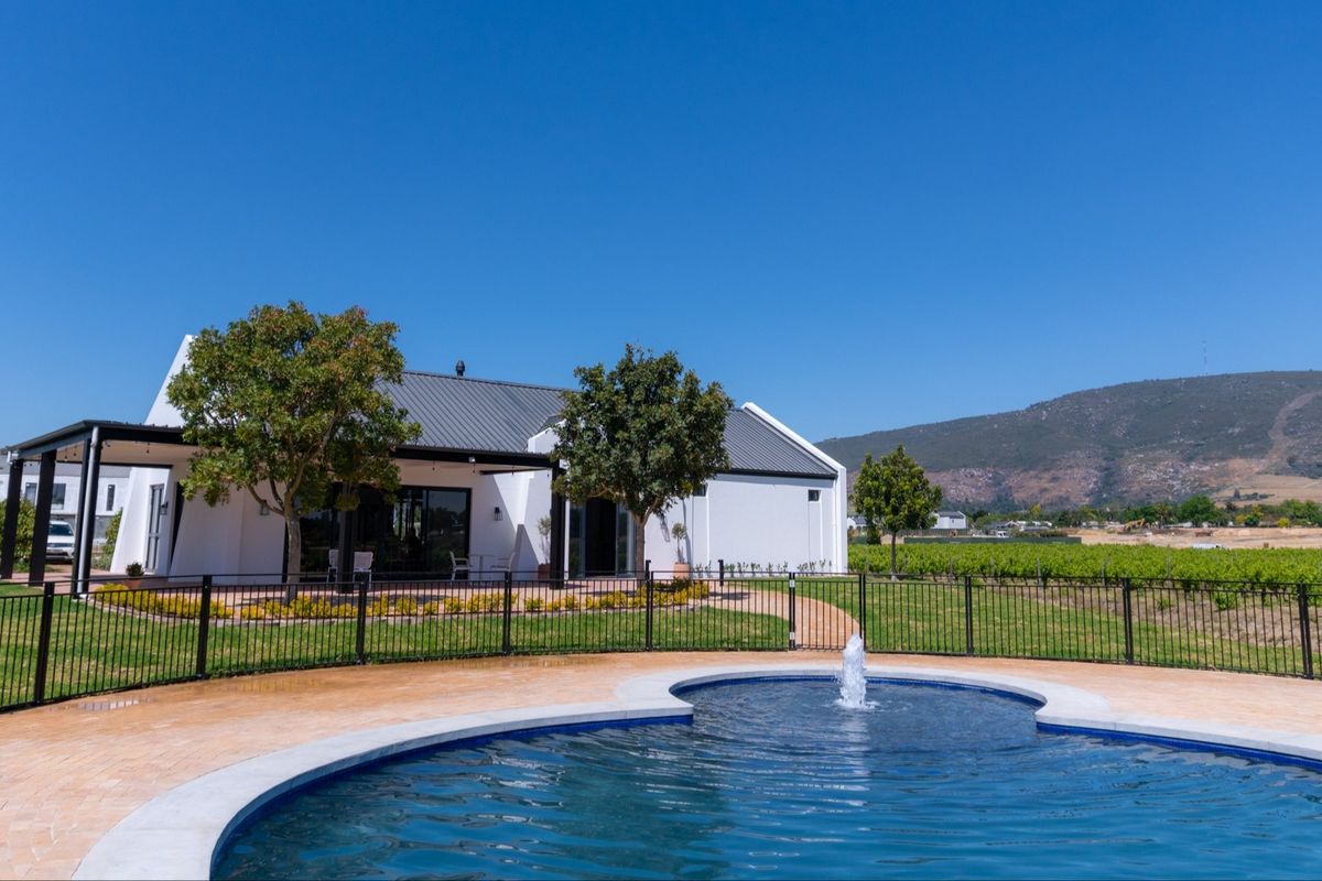 A well-maintained swimming pool with a central water fountain, set within a landscaped garden featuring a covered patio and scenic mountain views.