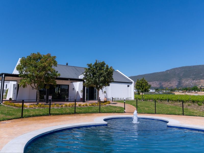 A well-maintained swimming pool with a central water fountain, set within a landscaped garden featuring a covered patio and scenic mountain views.