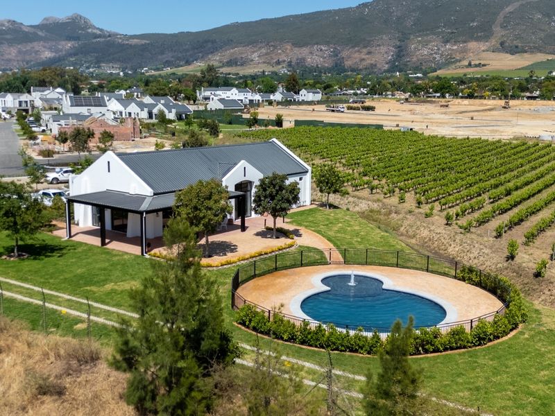 Aerial view of a modern residence featuring a swimming pool, covered patio, and expansive garden set against a scenic mountain backdrop.