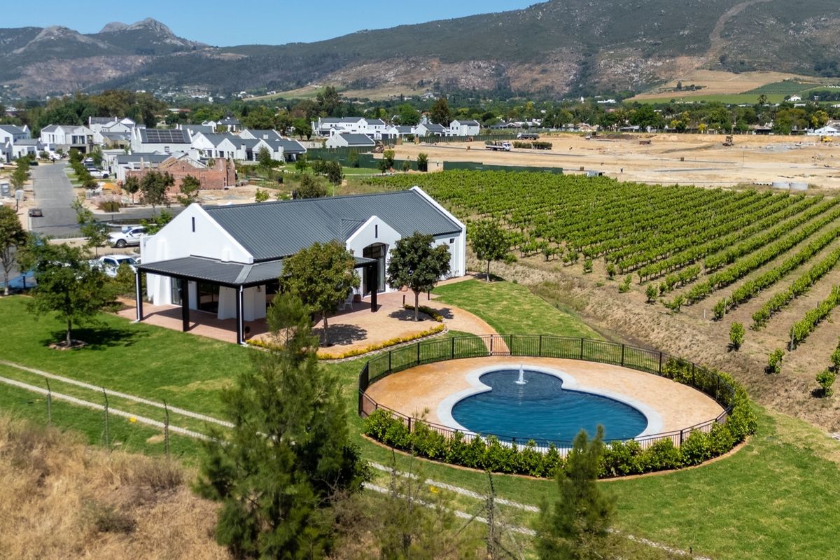 Aerial view of a modern residence featuring a swimming pool, covered patio, and expansive garden set against a scenic mountain backdrop.