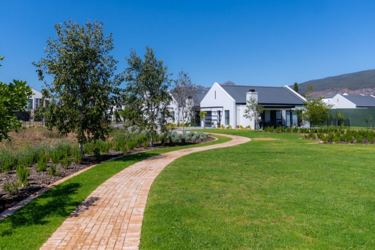 A well-maintained residential exterior featuring a brick pathway leading through a landscaped garden towards a modern house with a metal roof.