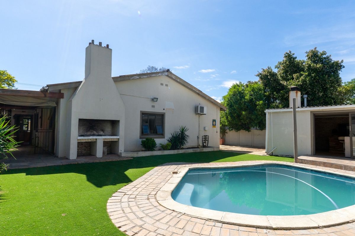 Rear garden area featuring a swimming pool, brick-paved surround, and a built-in outdoor braai area attached to the main house structure.