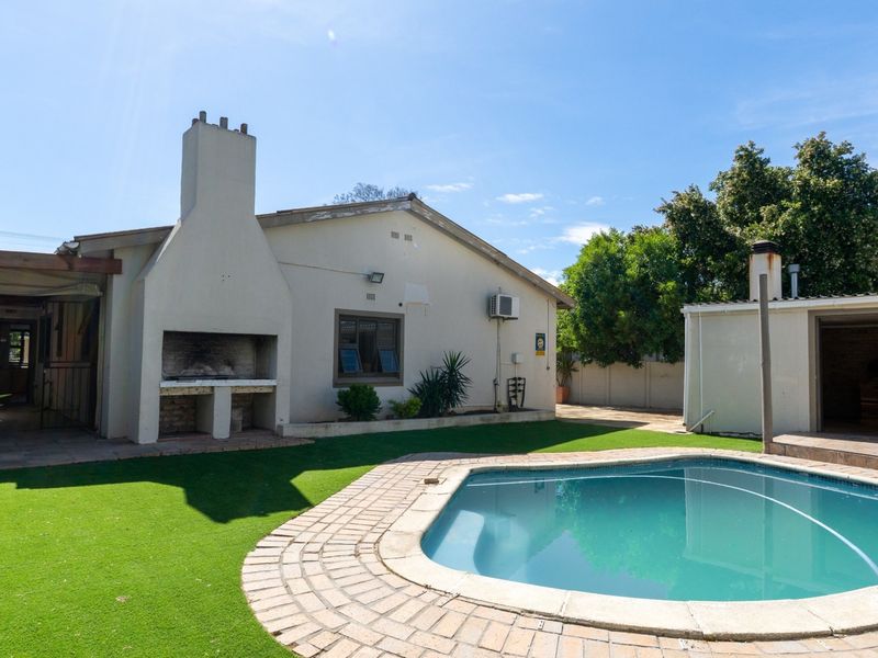 Rear garden area featuring a swimming pool, brick-paved surround, and a built-in outdoor braai area attached to the main house structure.