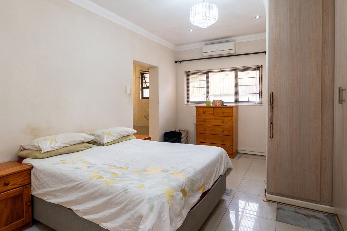 A bedroom featuring built-in cupboards, tiled flooring, and an air conditioning unit, with an adjoining en-suite bathroom area.