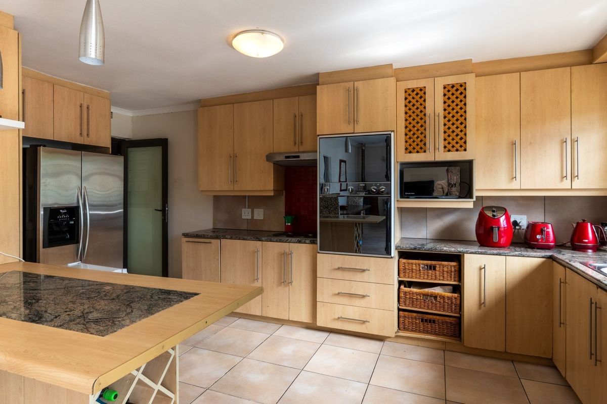 A functional kitchen featuring light wood cabinetry, granite countertops, built-in oven, extractor fan, and tiled flooring with an integrated breakfast nook.