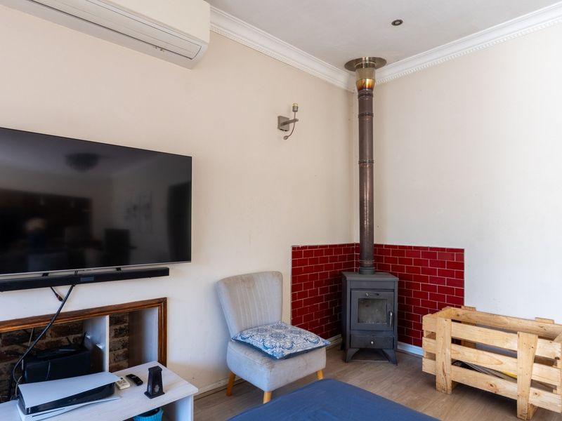 Living room featuring a wood-burning stove with a red tiled surround, wall-mounted air conditioning unit, and decorative coving.