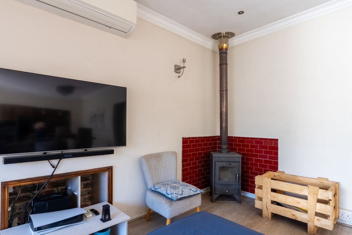 Living room featuring a wood-burning stove with a red tiled surround, wall-mounted air conditioning unit, and decorative coving.