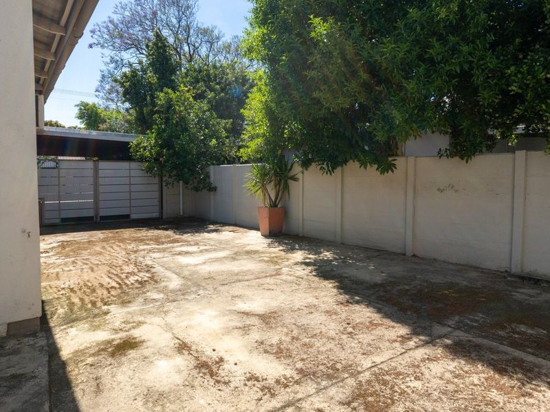 A paved driveway area featuring a precast concrete boundary wall and security gate, providing access to the property.