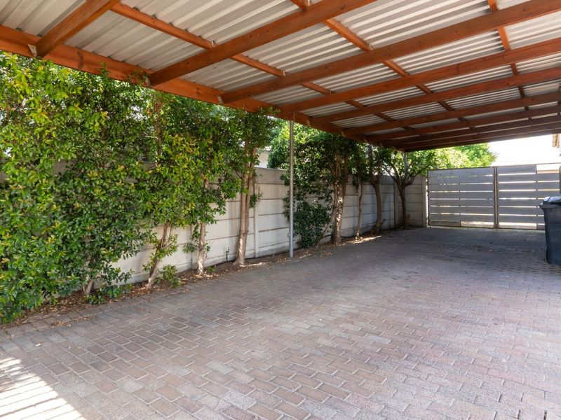 A covered carport area featuring a timber-framed roof structure, paved flooring, and secure perimeter walling with a metal gate.