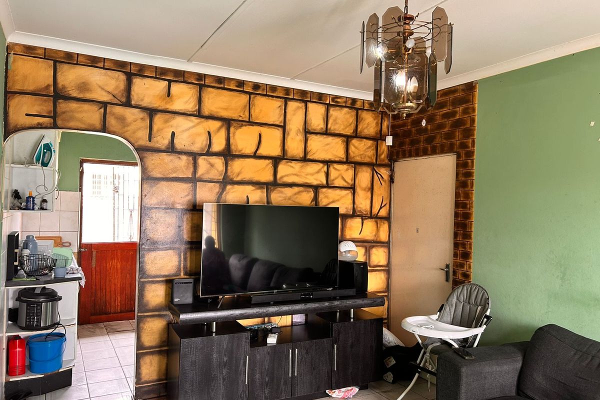 Living room featuring a decorative stone-effect feature wall, tiled flooring, and an arched doorway leading to the kitchen area.