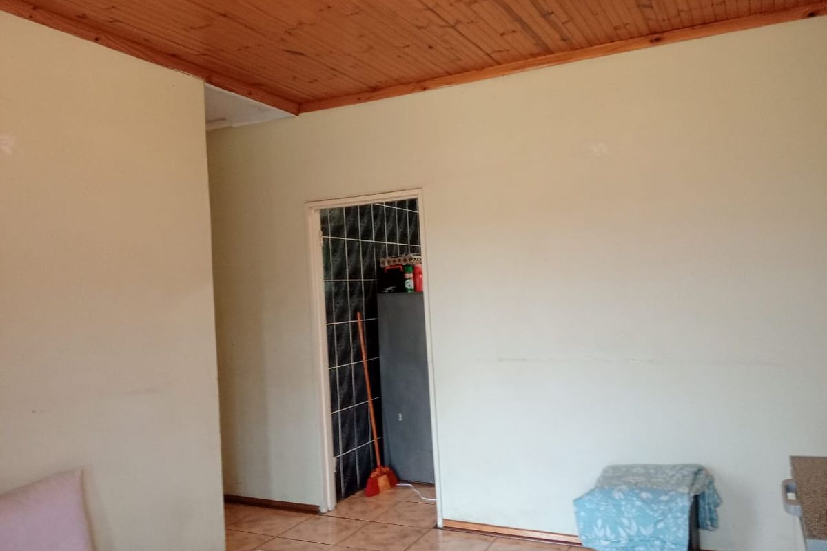An interior view showing a living area with tiled flooring and a timber-clad ceiling, leading into a tiled utility or kitchen space.