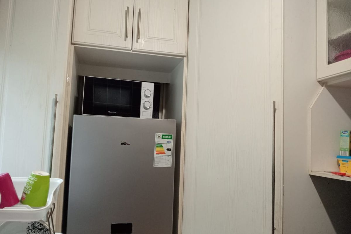 A kitchen storage area featuring built-in cabinetry with a dedicated alcove for a refrigerator and microwave.