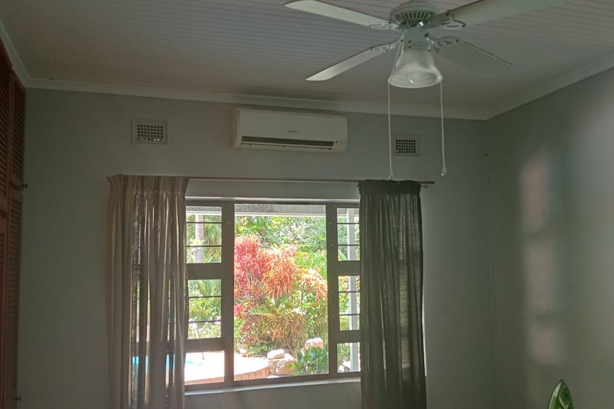 A bedroom featuring built-in wooden cabinetry, a ceiling fan, and a wall-mounted air conditioning unit, with a view overlooking the garden.
