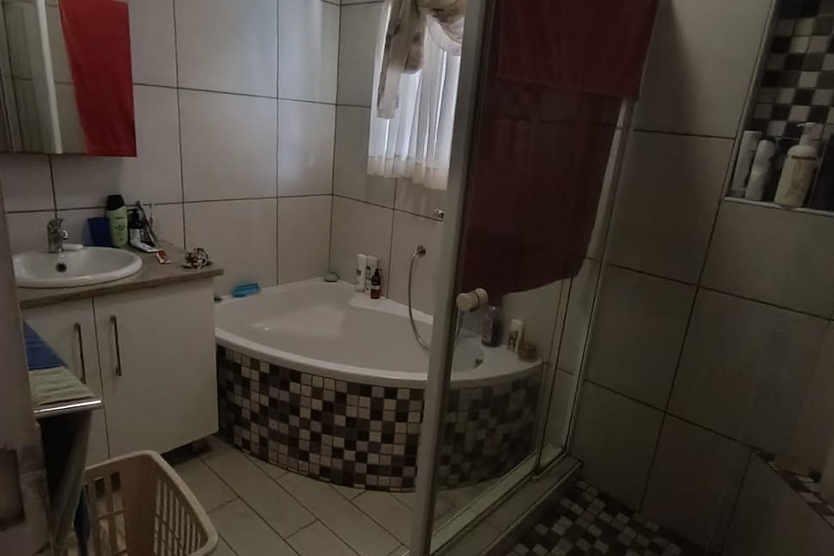 A functional bathroom featuring a corner bathtub, a separate glass-enclosed shower, and a vanity basin with tiled wall finishes.