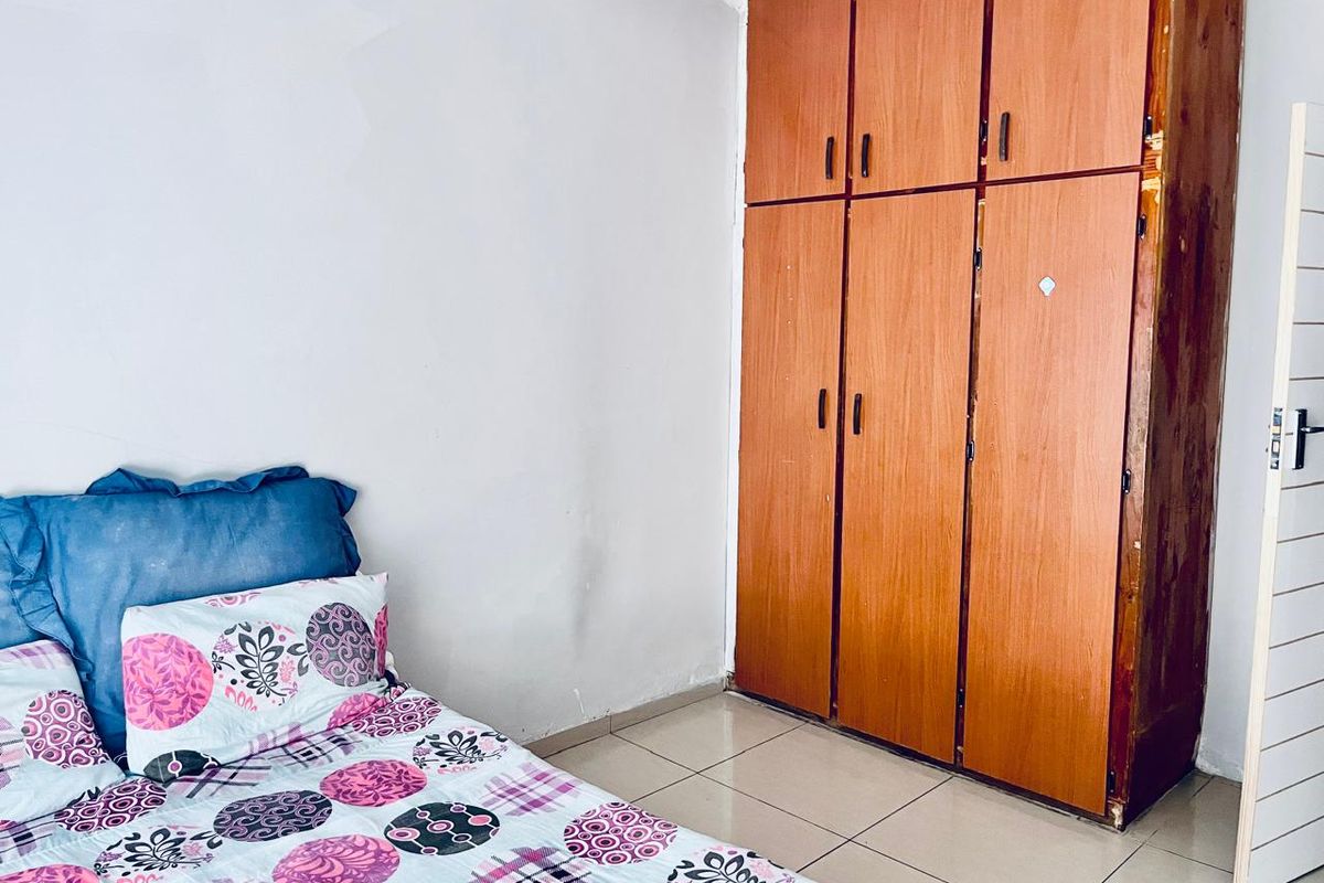 A bedroom featuring tiled flooring and a built-in wooden wardrobe with visible wear.