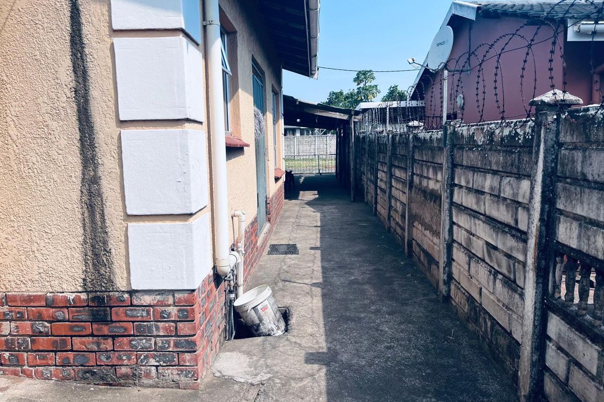 A narrow side passage of the house featuring a concrete walkway, boundary wall with security wire, and exterior wall finishes.