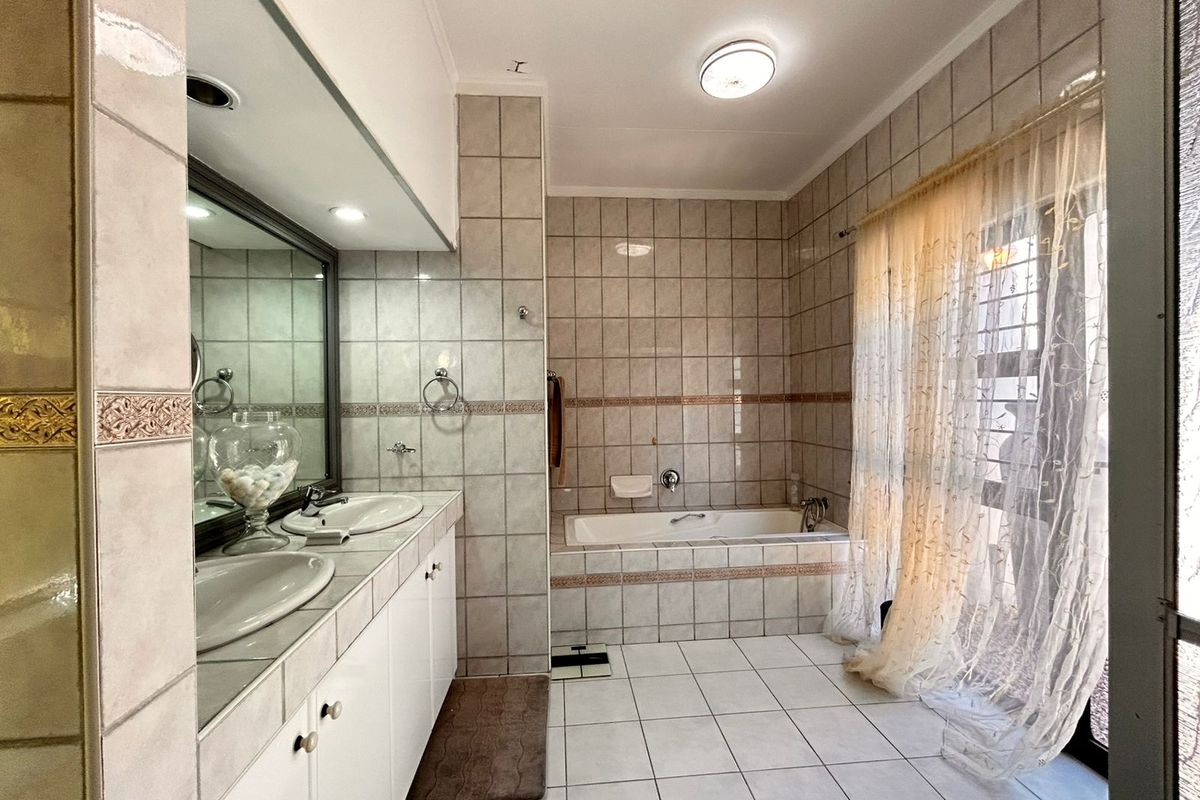 A functional bathroom featuring a double vanity with integrated sinks, a built-in bathtub, and floor-to-ceiling wall tiling.