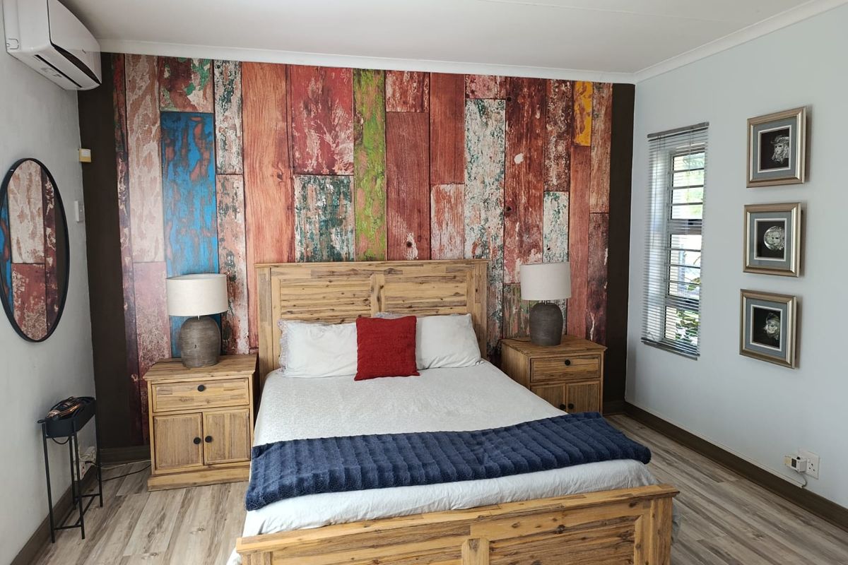 A well-maintained bedroom featuring a decorative wood-look feature wall, split-system air conditioning unit, and horizontal window blinds.
