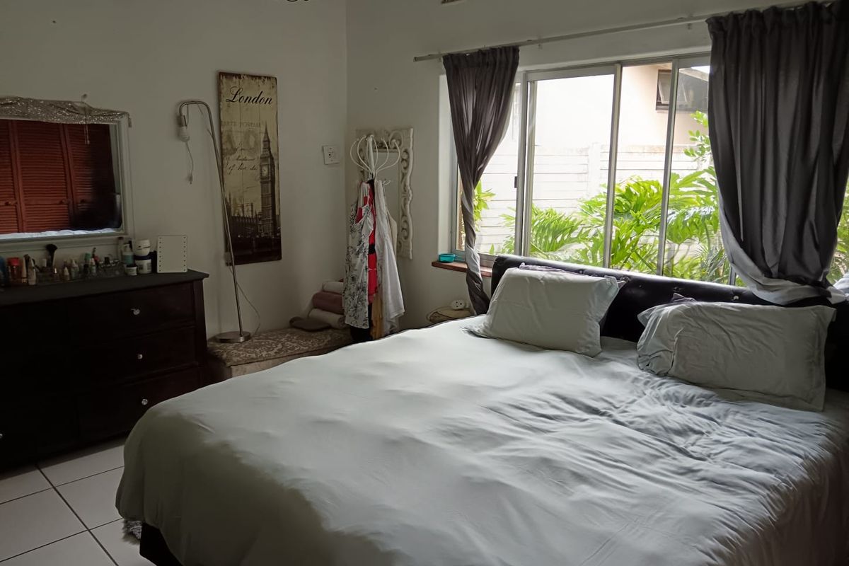 A bedroom featuring tiled flooring, a large sliding window with garden views, and a wall-mounted air conditioning unit.