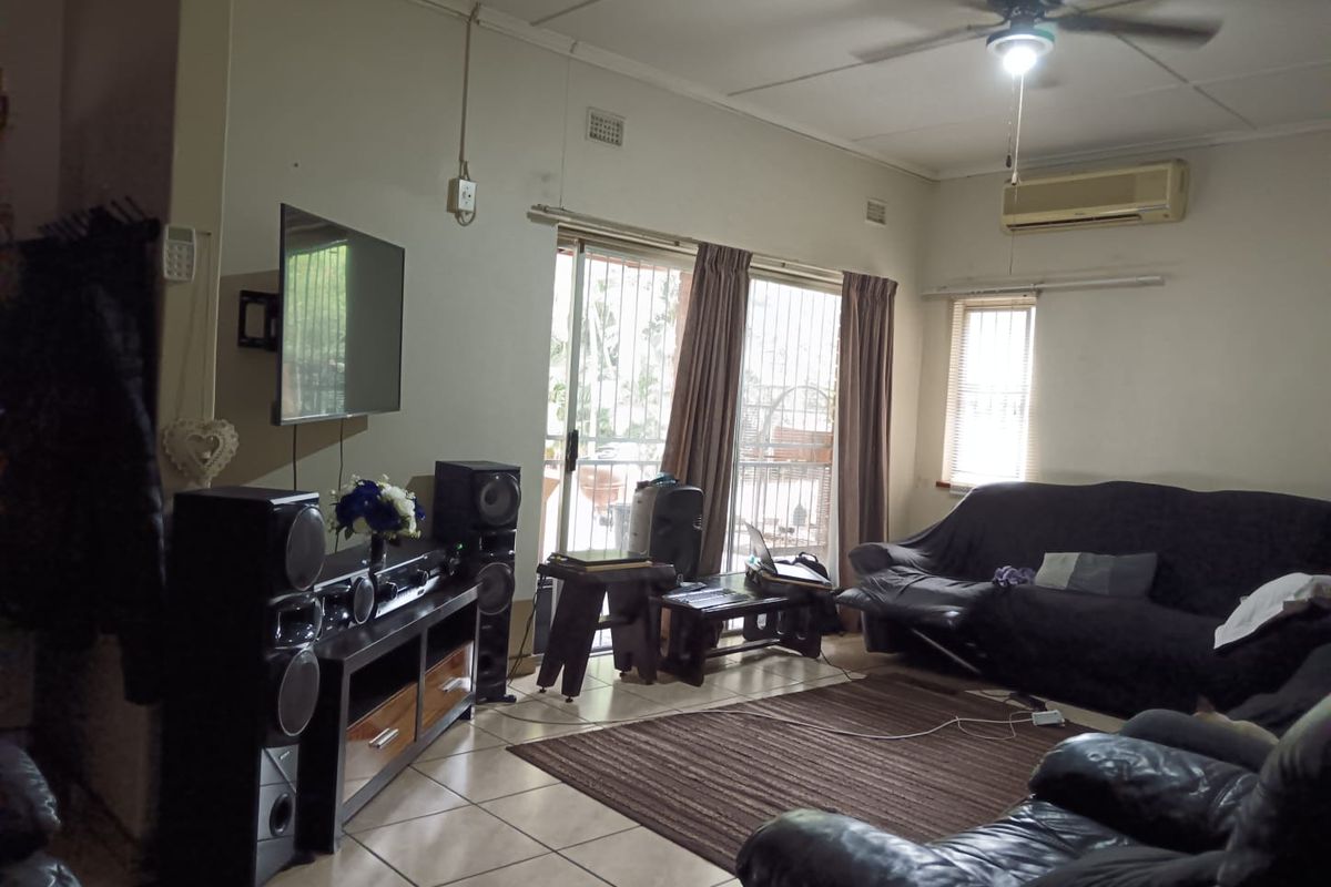A living room featuring tiled flooring, a ceiling fan, and a wall-mounted air conditioning unit with access to an outdoor area.