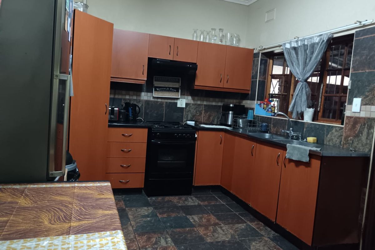 A functional kitchen featuring wood-tone cabinetry, dark tiled countertops, a built-in oven with extractor fan, and a double basin sink.