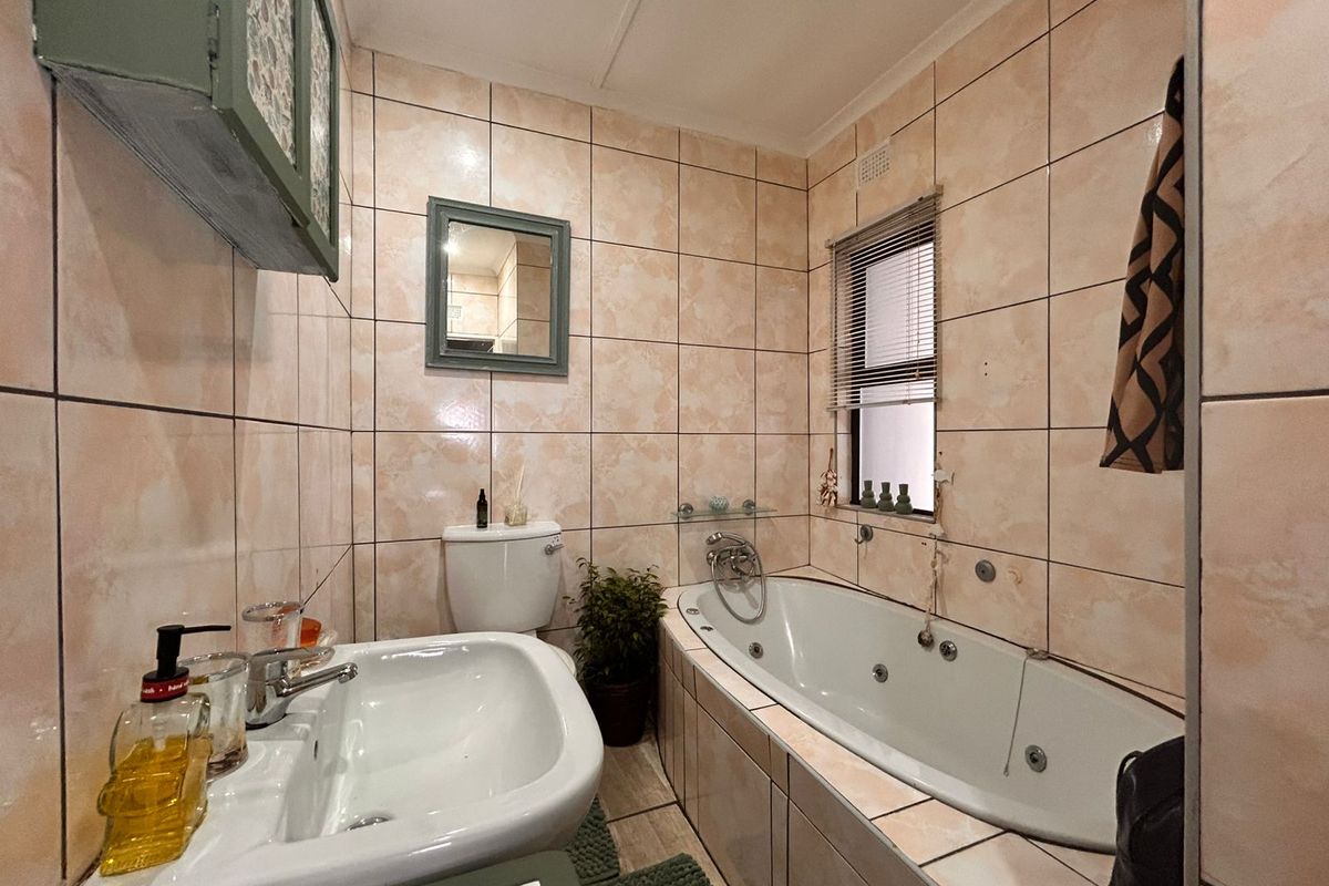 A functional bathroom featuring a built-in bathtub, pedestal basin, and toilet with full-height wall tiling.
