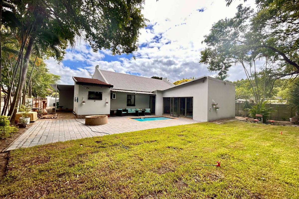 Rear view of the house featuring a paved patio area, a swimming pool, and a well-maintained garden with mature trees.