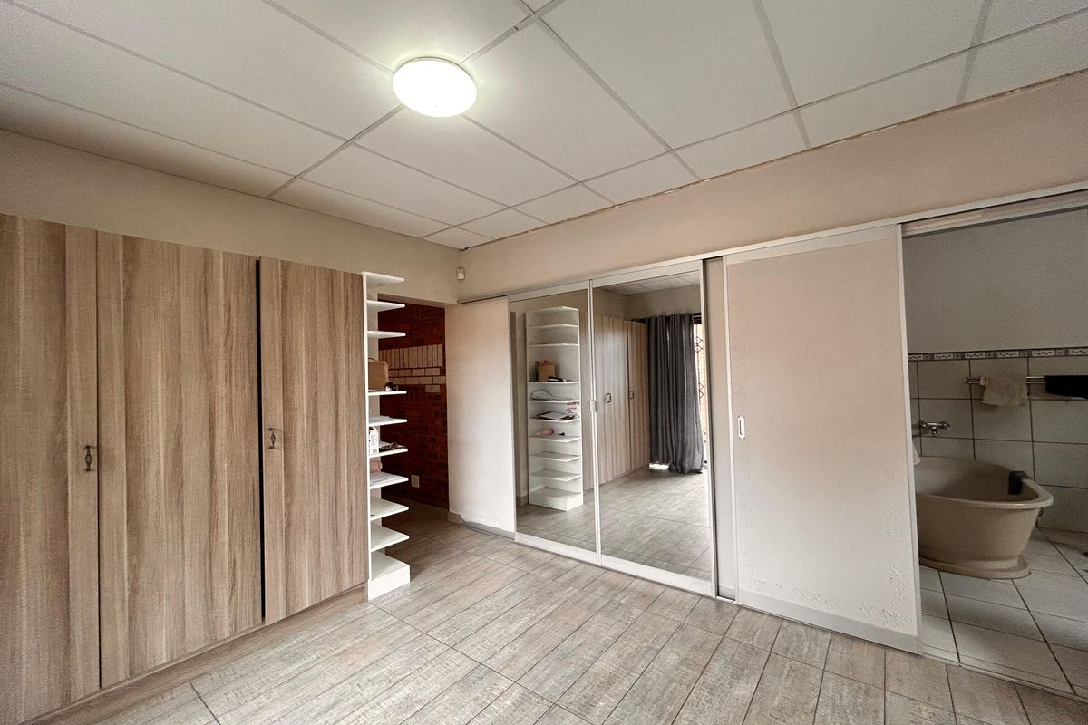 Bedroom featuring extensive built-in wooden cabinetry, mirrored sliding wardrobe doors, and direct access to an en-suite bathroom.