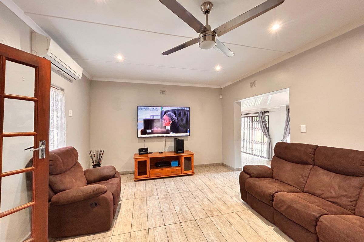 A well-maintained living room featuring tiled flooring, a ceiling fan, and a wall-mounted air conditioning unit, providing a comfortable and functional living space.