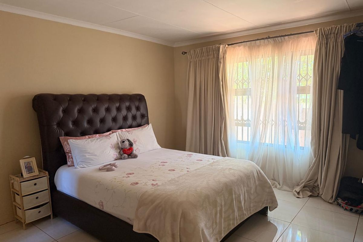 A well-lit bedroom featuring tiled flooring, neutral wall tones, and a large window with security bars, providing a comfortable and functional living space.