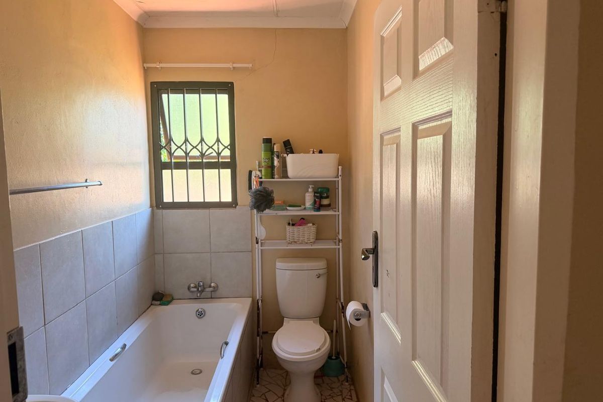 A functional bathroom featuring a built-in bathtub, toilet, and security bars on the window, providing essential utility in a compact layout.
