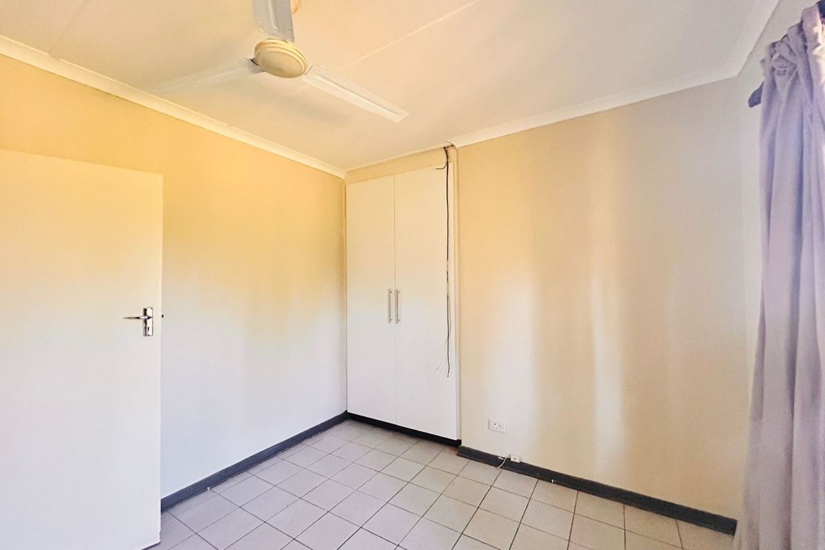A simple bedroom featuring tiled flooring, a built-in wardrobe, and a ceiling fan.