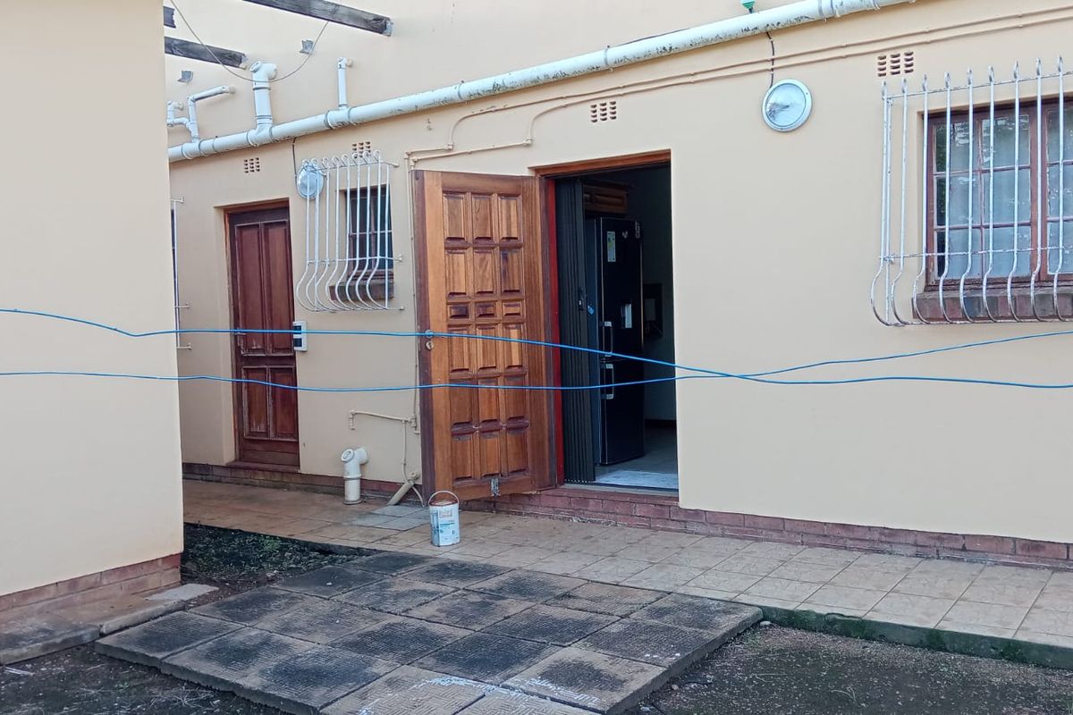 Exterior view of an apartment entrance featuring tiled patio area, wooden doors, and security bars on windows.