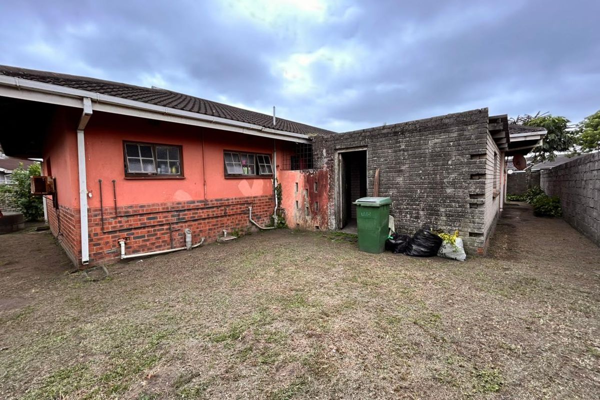 Rear exterior view of the property featuring a brick and painted facade with a small yard area and utility access.
