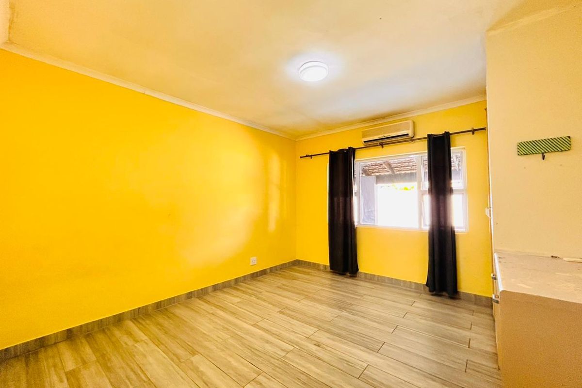 A bedroom featuring wood-look tile flooring, bright yellow walls, a wall-mounted air conditioning unit, and a window with curtain rod.