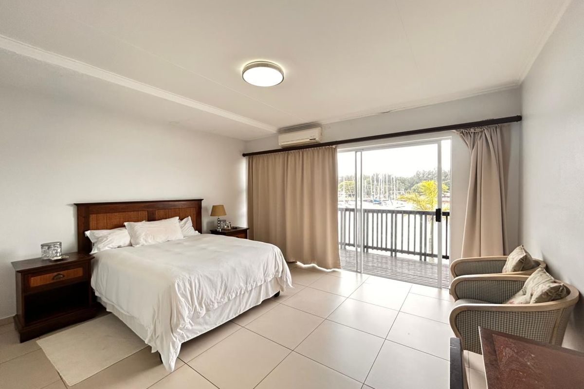 Spacious bedroom featuring tiled flooring, a wall-mounted air conditioning unit, and sliding glass doors opening onto a private balcony with marina views.
