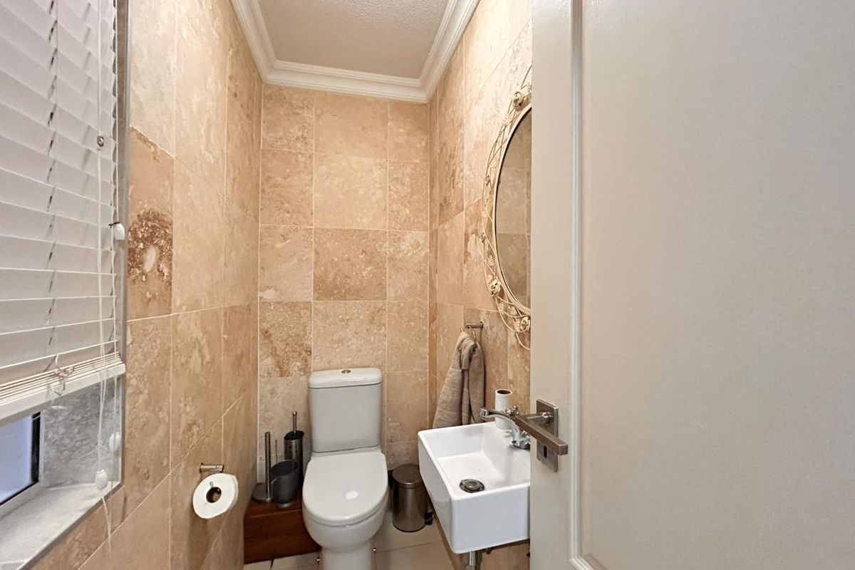 A compact guest bathroom featuring floor-to-ceiling stone wall tiles, a wall-mounted basin, and a modern toilet.