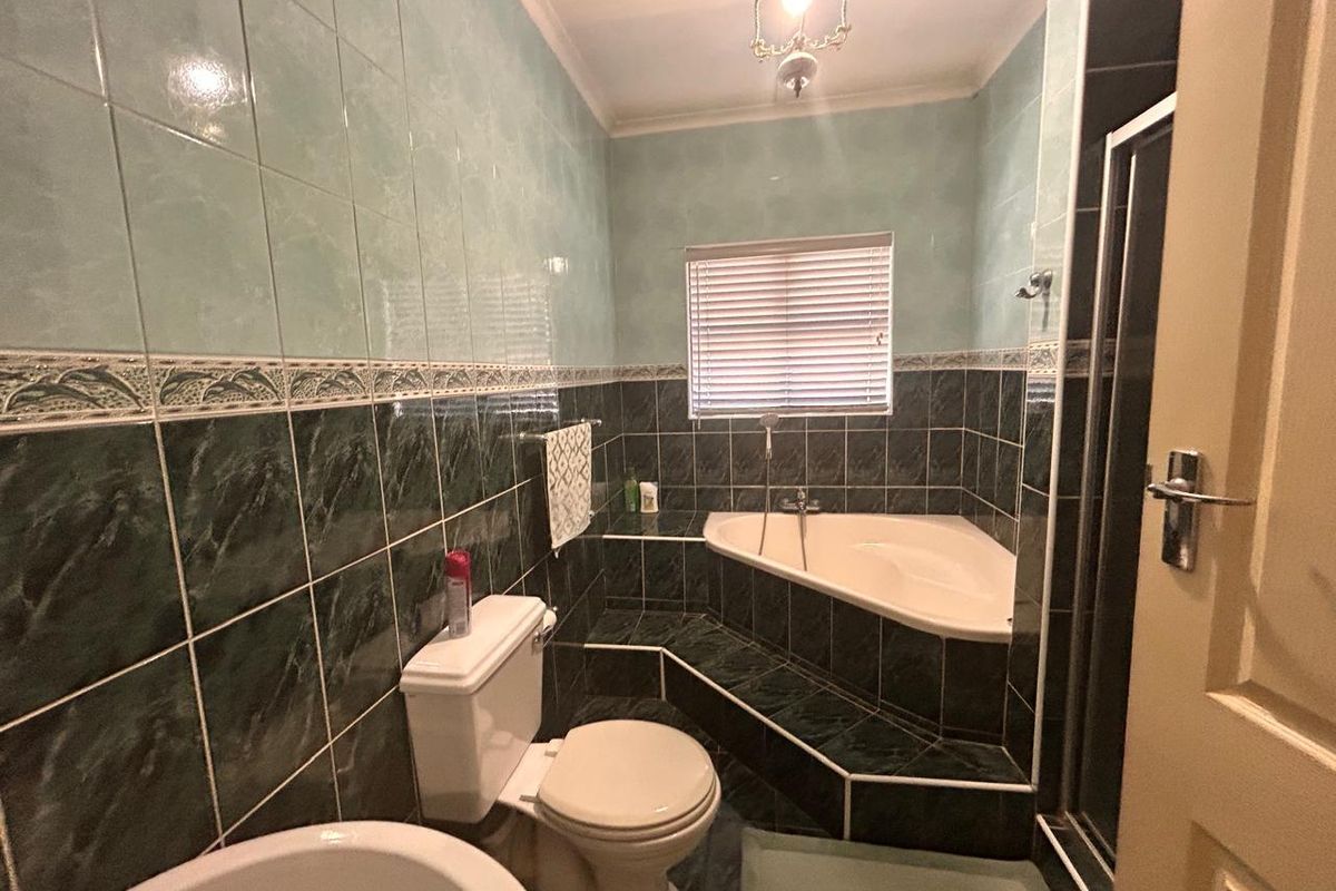 A functional bathroom featuring a corner bathtub, tiled surround, and standard sanitary ware with a classic layout.
