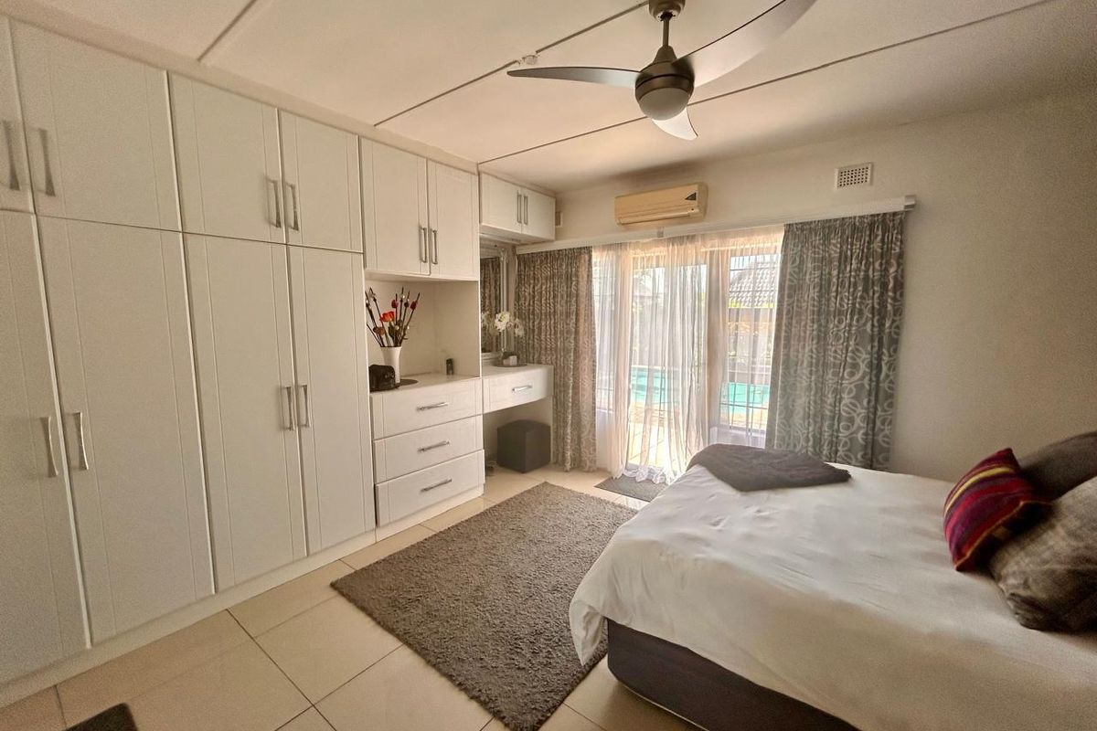 A well-maintained bedroom featuring extensive built-in cabinetry, a ceiling fan, air conditioning unit, and sliding glass doors providing access to the pool area.