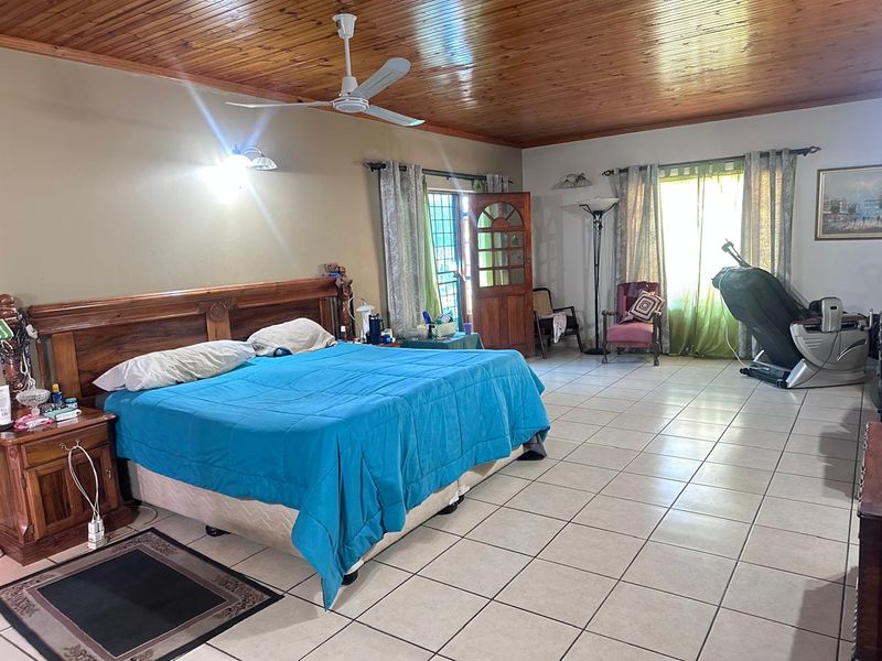 Spacious bedroom featuring ceramic floor tiles and a warm timber tongue and groove ceiling with an integrated ceiling fan.