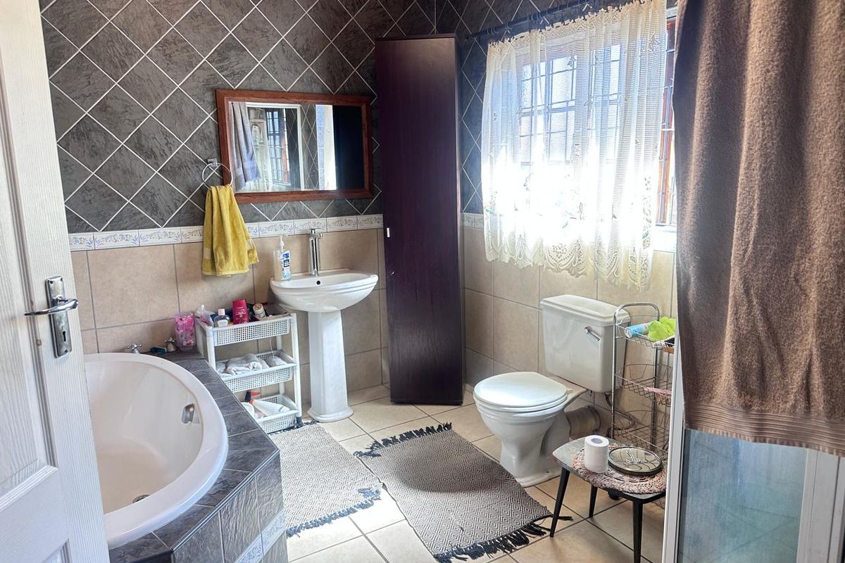A functional bathroom featuring a pedestal basin, built-in bathtub, and toilet, finished with tiled walls and flooring.