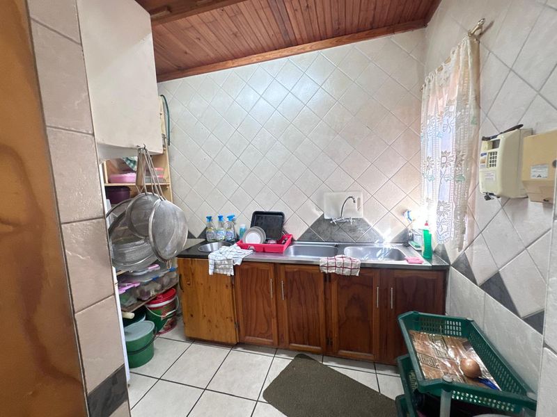 A functional scullery area featuring wooden cabinetry, a double stainless steel sink, tiled splashbacks, and a timber-clad ceiling.